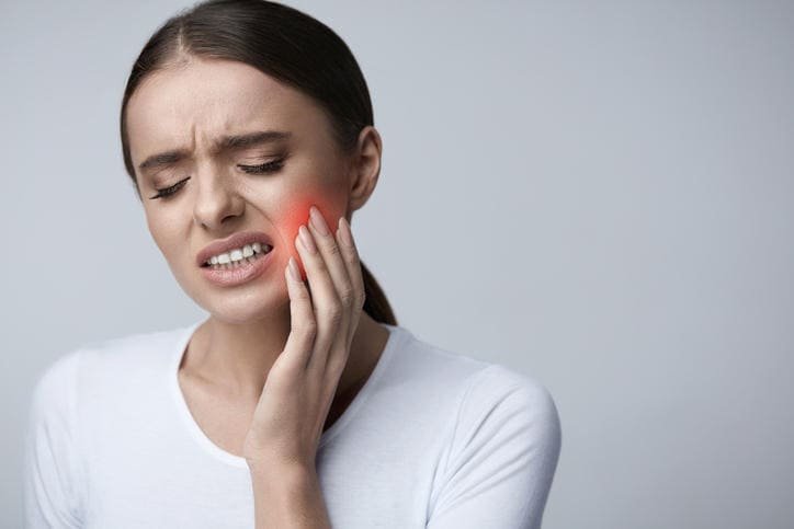 Donna con forte mal di denti che si tocca la guancia per il dolore, urgenza dentistica ad Acqui Terme